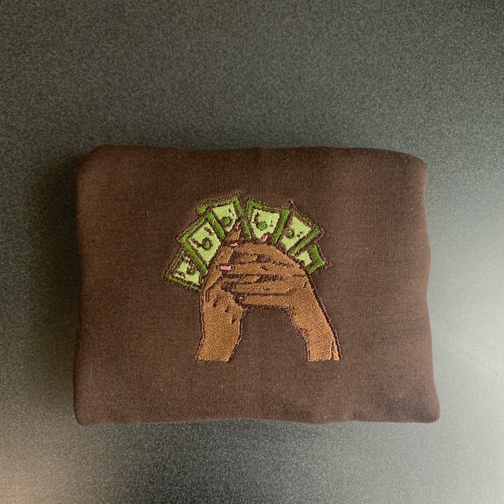 Embroidered crewneck brown skin hands hold money